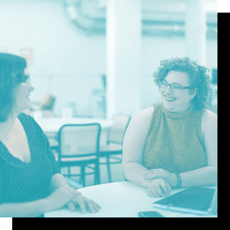 two women talking at a table with a laptop